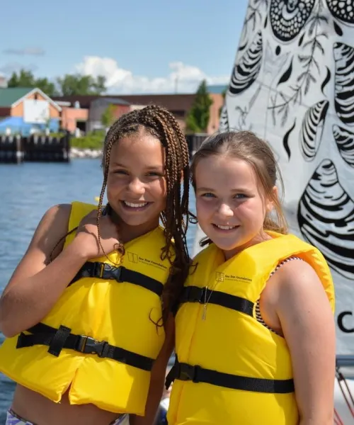 two kids in yellow personal flotation devices on a sailboat on Lake Champlain